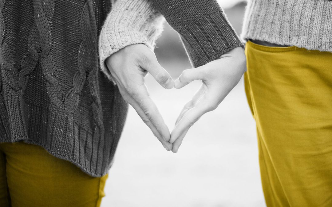 Black and white photo of a couple making a heart shape with their hands at a marketing workshop.