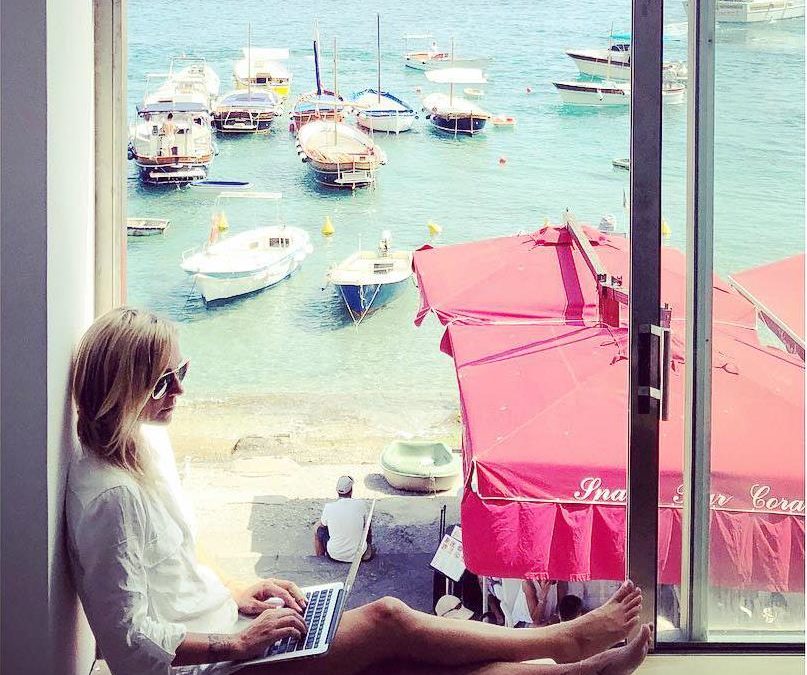 A woman participating in a marketing workshop, sitting on a window sill with a laptop.